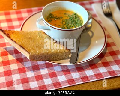 Eine Schüssel Tomatensuppe garniert mit Petersilie, serviert mit einer Scheibe Knoblauchbrot auf einem weißen Teller auf einer roten karierten Tischdecke in Lübeck. Stockfoto