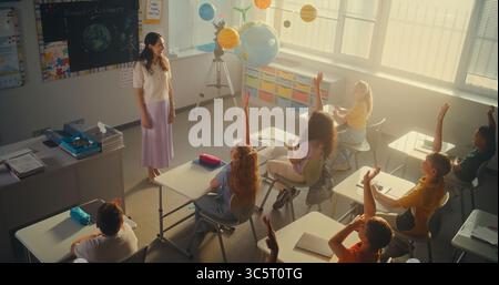 MINT-Klasse: Lehrerin für Ökologie für Grundschüler im Klassenzimmer. Diverse Kinder heben die Hände, um Antworten zu geben, Smart Girl geht in den Vorstand und stellt Hausaufgaben vor. Hoher Winkel. Stockfoto