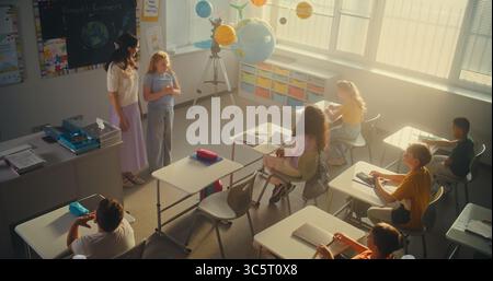 MINT-Klasse: Lehrerin für Ökologie für Grundschüler im Klassenzimmer. Diverse Kinder heben die Hände, um Antworten zu geben, Smart Girl geht in den Vorstand und stellt Hausaufgaben vor. Hoher Winkel. Stockfoto