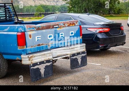 Medora, ND, USA - 17. Juli 2025: Ein rostiger Ford Pickup-Truck steht neben einem eleganten, modernen Auto Stockfoto