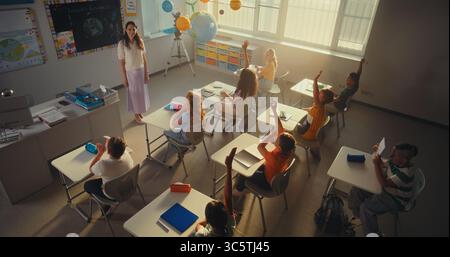 Lehrerin unterrichtet Kinder während des umweltwissenschaftlichen Unterrichts im modernen Klassenzimmer. Kluge Kinder heben die Hände, Grundschulmädchen zeigt Wissen über Ökologie vor der Klasse. Hoher Winkel. Stockfoto