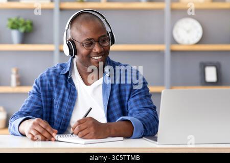 E-Education. Happy schwarz reifen Mann mit Laptop und Notizen, Hören Online-Kurs Stockfoto