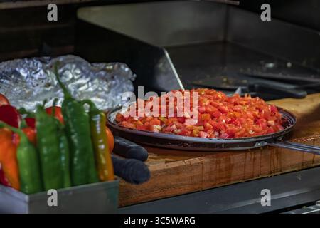 Frisch geschnittene rote Tomaten und grüne Chili-Paprika sitzen auf einem hölzernen Schneidebrett und werden in einem authentischen Kebab-Restaurant in Istanbul, Türkei, zubereitet Stockfoto