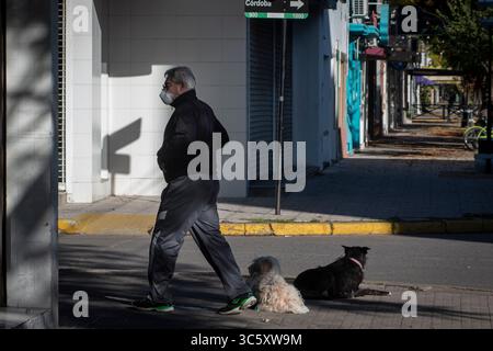 14. April 2020, Firmat, Santa Fe, Argentinien: Ein Mann mit Gesichtsmaske geht an zwei Hunden vorbei, die vor einer Apotheke ruhen. Die Verwendung von Gesichtsmasken in allen öffentlichen Räumen ist in der Stadt seit dem 13. April verpflichtend. Aufgrund des Mangels an medizinischen Vorräten raten Behörden die Verwendung von hausgemachten Gesichtsmasken, um chirurgische Masken für Gesundheitspersonal zu halten. (Bild: © Patricio Murphy/ZUMA Wire) Stockfoto