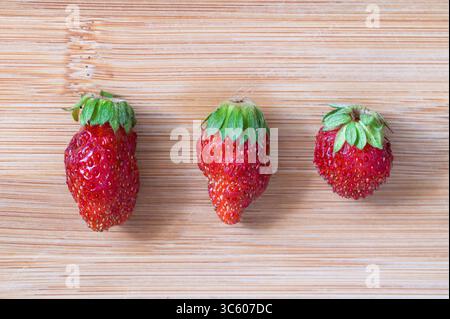 Drei Erdbeeren in einer Linie auf einem Holzhintergrund Stockfoto