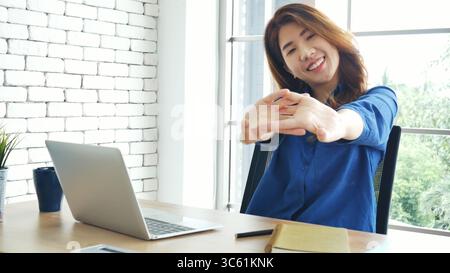 Frau streckt den Arm hoch und sitzt falsch in der Position des Home Office-Schreibtisches. Rückseite einer jungen asiatischen Frau müde von der Arbeit Körper Stress Rücken Schmerz Büro Sy Stockfoto