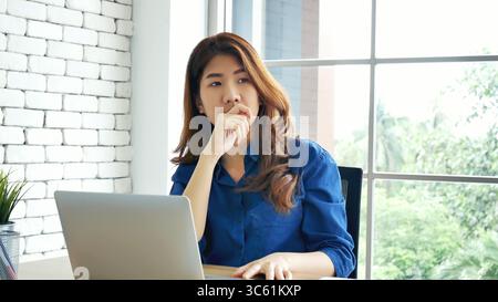 Frau streckt den Arm hoch und sitzt falsch in der Position des Home Office-Schreibtisches. Rückseite einer jungen asiatischen Frau müde von der Arbeit Körper Stress Rücken Schmerz Büro Sy Stockfoto