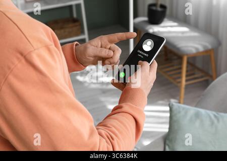 Junger Mann, der das Handy hält und zu Hause einen Anruf auf dem Bildschirm eingeht Stockfoto