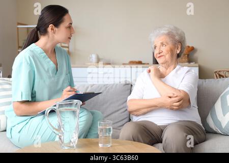 Physiotherapeutin schreibt in Zwischenablage mit Seniorin zu Hause Stockfoto