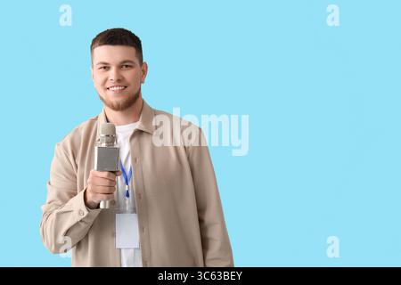 Männlicher Reporter mit Mikrofon und leerem Namensschild auf blauem Hintergrund Stockfoto