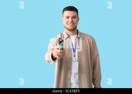 Männlicher Reporter mit Mikrofon und leerem Namenslappen, der ein Interview auf blauem Hintergrund macht Stockfoto
