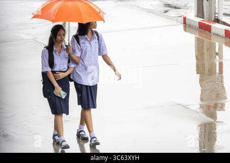 SAMUT PRAKAN, THAILAND, 27. JUNI 2025, gehen zwei Mädchen in Schuluniformen unter einem Regenschirm auf einer regnerischen Straße Stockfoto