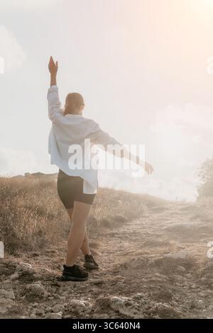 Mann, Tanz, Sonnenuntergang - Ein Mann in einem weißen Hemd tanzt auf einem felsigen Hügel mit einem Sonnenuntergang im Hintergrund. Stockfoto