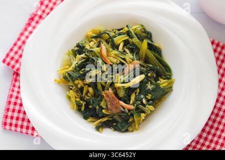 Nahaufnahme eines Tellers mit gebratenem Gemüse im Manado-Stil (Kangkung Bunga Pepaya) mit frischen, belaubten Zutaten und aromatischen Gewürzen. Stockfoto
