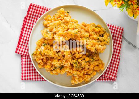 Eine Portion frisch gebratener Corn Fritters (Bakwan Jagung), Golden und knusprig, serviert auf einem weißen Teller mit einem karierten Tuch. Stockfoto