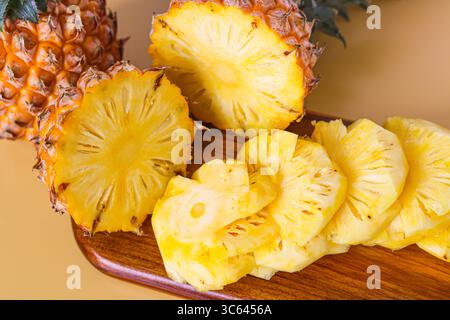 Nahaufnahme einer frisch geschnittenen Ananas auf einem hölzernen Schneidebrett, hinter der eine ganze Ananas steht für eine lebendige tropische Präsentation. Stockfoto