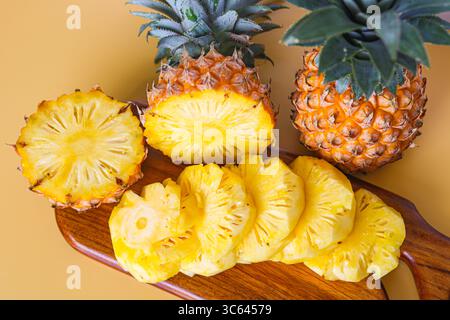 Frisch geschnittene Ananas auf einem hölzernen Schneidebrett angeordnet, mit einer ganzen Ananas dahinter für eine lebendige tropische Präsentation. Stockfoto