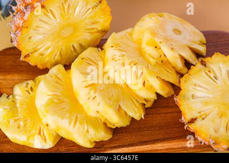 Frisch geschnittene Ananasscheiben, kunstvoll auf einem Holzschneidebrett angeordnet, sorgen für eine lebendige tropische Präsentation. Stockfoto