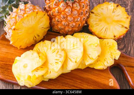 Nahaufnahme der frisch geschnittenen Ananas auf einem hölzernen Schneidebrett, mit einer ganzen Ananas hinter der Tür für eine lebendige tropische Präsentation. Stockfoto