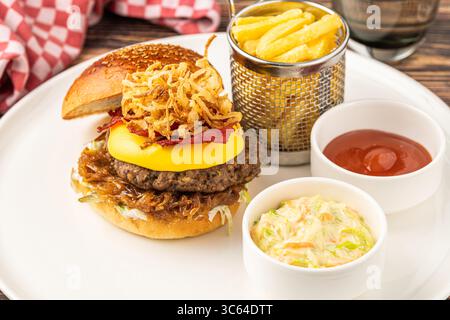 Köstlicher Gourmet-Burger mit Cheddar-Käse, gebratenen Zwiebeln, Krautsalat und Pommes frites Stockfoto