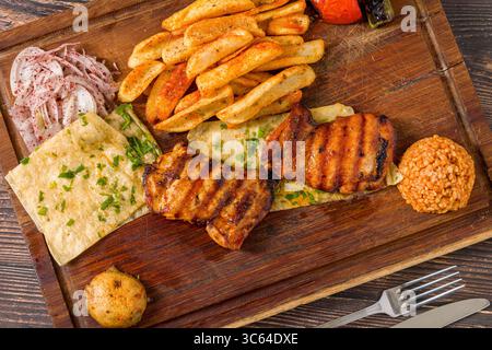 Gegrilltes Hähnchenkotelett ohne Knochen, serviert mit Pommes, Lavash, Zwiebeln und Bulgur Stockfoto