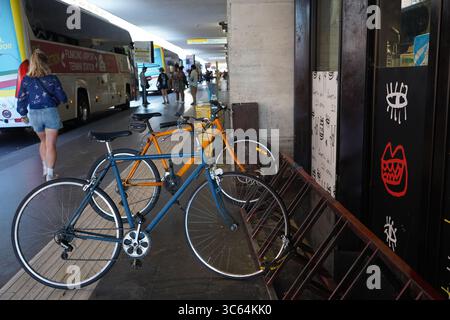 Vor dem Terminal des Flughafens Fiumicino stehen Fahrräder an, während Reisende vorbeifahren und die Busse im Hintergrund warten, was sowohl den nah- als auch den Fernverkehr miteinander verbindet. Stockfoto