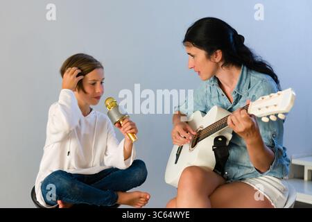 Eine Mutter und Tochter nehmen einen musikalischen Moment ein. Das Mädchen hält ein Mikrofon und singt anscheinend zur Gitarre ihrer Mutter. Ein herzerwärmendes Gefühl Stockfoto