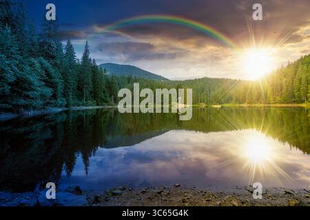 Abgelegene Berglandschaft mit Waldsee zur Sommersonnenwende. Reisen Sie mit Sonne und Mond in die Natur. Malerischer Blick auf die Reflexion der Nadelbäume Stockfoto