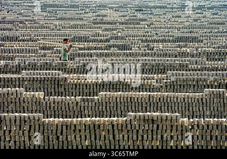 Gokul, Bangladesch - 12. Juli 2017: Blick auf einen Arbeiter, der einen Holzbalken in riesigen Ziegelsteinen trägt, wodurch eine strukturierte Landschaft aus Schatten und Erdtönen entsteht. Stockfoto