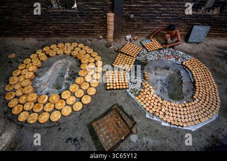 Bogura, Bangladesch - 5. Februar 2022: Blick auf einen Arbeiter, der sorgfältig frisch gebackene Waren um einen traditionellen Ofen herum arrangiert und ein warmes, goldenes Tableau in der rustikalen Backsteinkulisse schafft. Stockfoto