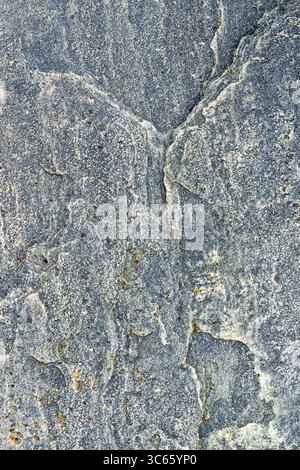 Aus nächster Nähe sehen Sie eine raue Steinoberfläche mit blaugrauer Farbe, Rissen und Mineralablagerungen unter natürlichem Licht. Stockfoto