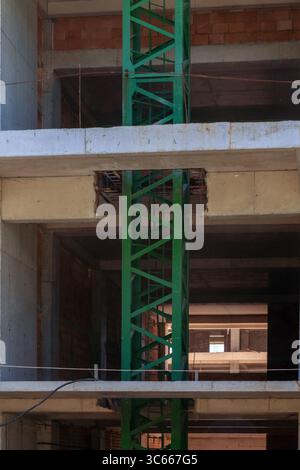 Vertikale Ansicht eines grünen Kranturms, der durch die Betonböden eines im Bau befindlichen unfertigen Gebäudes ragt. Stockfoto