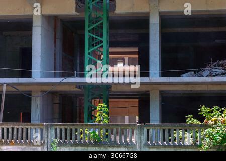 Blick in das Innere eines im Bau befindlichen mehrstöckigen Betongebäudes mit Stützbalken, Trümmern und einem grünen Kranturm. Stockfoto