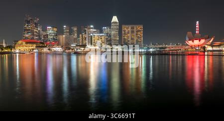 Singapur, Singapur - 19. Juni 2025: Blick auf die Skyline der Stadt bei Nacht, ihre Lichter schimmern und reflektieren von den ruhigen Gewässern, und das ArtScience Museum leuchtet rot. Stockfoto