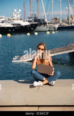 Lächelnde, schöne Frau mit Laptop am Pier im Hafen von Valencia, Spanien Stockfoto