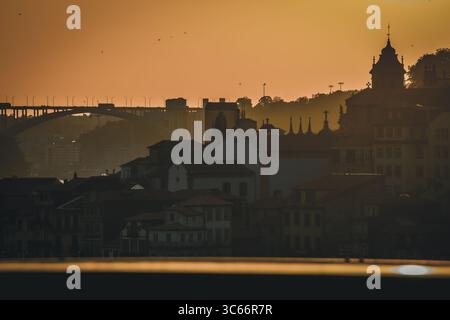 Porto, Portugal - 17. Juni 2022: Blick auf die Brücke Dom Luís i und die Skyline der Stadt in warmen, goldenen Tönen der untergehenden Sonne. Stockfoto
