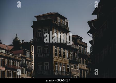Porto, Portugal - 17. Juni 2022: Blick auf verwitterte Gebäude, deren verzierte Fenster den Himmel reflektieren, während Schatten über die Fassaden tanzen. Stockfoto