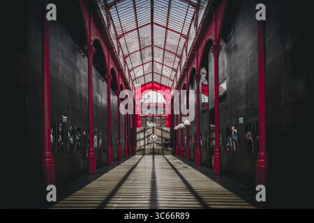 Porto, Portugal - 17. Juni 2022: Blick auf die leuchtend roten Säulen und die Glasdecke des Bolhão Markts, die lange Schatten auf dem kühlen, glatten Boden wirft. Stockfoto