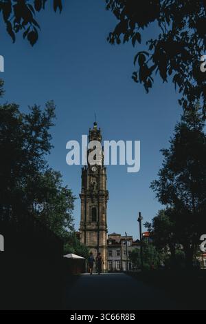 Porto, Portugal - 17. Juni 2022: Blick auf den Kirchturm Clerigos, der in den hellblauen Himmel ragt, eingerahmt von dem dunkelgrünen Laub der umliegenden Bäume. Stockfoto
