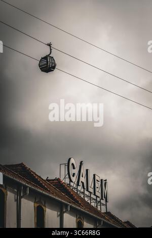 Porto, Portugal - 17. Juni 2022: Blick auf eine Seilbahn, die lautlos über dem Galex-Gebäude gleitet, vor dem Hintergrund des grausamen, bewölkten Himmels. Stockfoto