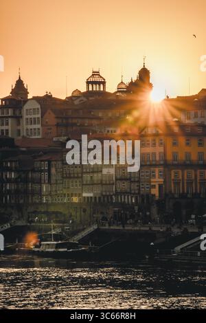 Porto, Portugal - 17. Juni 2022: Blick auf die Skyline der Stadt im goldenen Licht, beleuchtet historische Gebäude und wirft lange Schatten über den Fluss Douro. Stockfoto