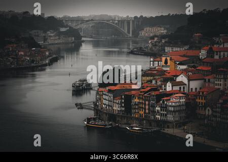 Porto, Portugal - 17. Juni 2022: Blick auf die Terrakottadächer, die zum Fluss Douro herabfallen und den gedämpften Himmel und die entfernte Arrábida-Brücke reflektieren. Stockfoto