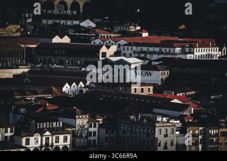 Porto, Portugal - 17. Juni 2022: Blick auf die Dächer der Stadt, wo sich die berühmten Schilder „Sandeman“ und „WOW“ von den Terrakottafliesen und schattigen Gebäuden abheben. Stockfoto
