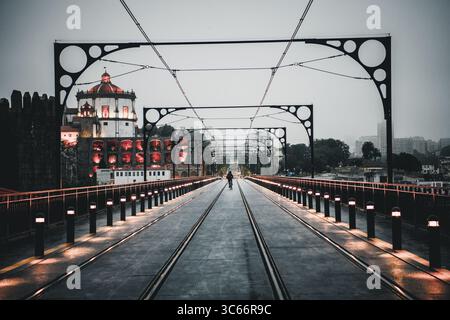 Porto, Portugal - 17. Juni 2022: Blick auf die Brücke Dom Luís i, deren Eisenbögen die beleuchtete Architektur der Stadt vor einem gedämpften Himmel umrahmen. Stockfoto