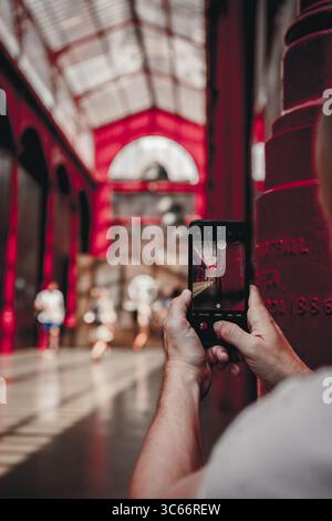 Porto, Portugal - 17. Juni 2022: Blick auf eine Person, die die leuchtenden Rottöne der Architektur des berühmten Bahnhofs São Bento mit ihrem Smartphone festnimmt. Stockfoto
