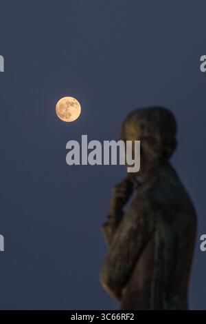 Porto, Portugal - 17. Juni 2022: Blick auf eine Bronzestatue, die nachdenklich den leuchtenden Vollmond im tiefblauen Dämmerhimmel betrachtet. Stockfoto