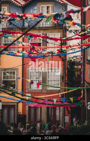 Porto, Portugal - 17. Juni 2022: Blick auf lebendige Gebäude, die mit bunten Luftschlangen geschmückt sind und Schatten auf der belebten Straße darunter werfen. Stockfoto