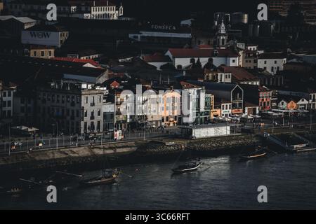 Porto, Portugal - 17. Juni 2022: Blick auf die farbenfrohen Fassaden des Viertels Ribeira, die zum Fluss Douro hinabragen, wo Boote sanft im dunklen Wasser abtauchen. Stockfoto