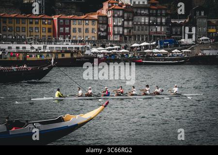 Porto, Portugal - 17. Juni 2022: Blick auf ein Ruderteam, das über den Fluss Douro gleitet, das pulsierende Viertel Ribeira vor farbenfroher Kulisse. Stockfoto
