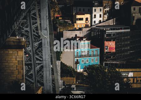 Porto, Portugal - 17. Juni 2022: Blick auf das leuchtend blaue Gebäude zwischen den Dächern, mit dem grauen Metallrahmen der Brücke, der einen industriellen Aspekt verleiht. Stockfoto